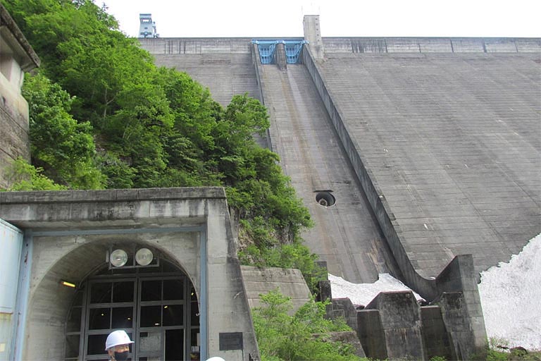 搬入口はダムの外部からトラックなどで資材を運搬し、天井クレーンで吊り上げて、発電機に必要な資材の上げ下ろしを行なう場所です。この搬入口からダムの外に出て見上げると、ダムの大きさがわかります。まだ雪が残っていますね。